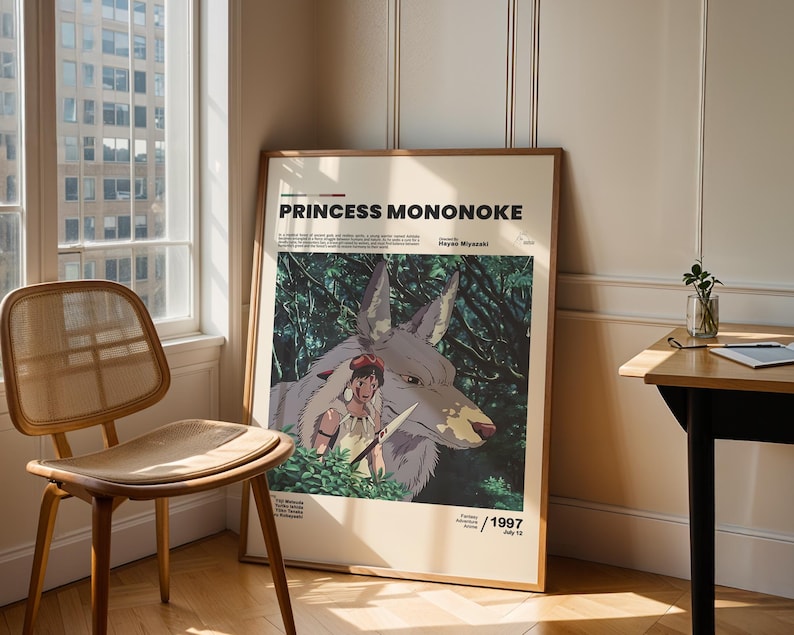 May include: A framed poster for the animated film "Princess Mononoke" featuring a wolf and a female character with a knife. The poster has the film's title in bold text and the year 1997. The poster is leaning against a wall next to a window and a wooden chair.