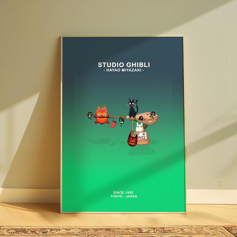 May include: A framed poster featuring Studio Ghibli characters on a gradient green and blue background. The poster includes a broom with black cats, a white cat, and a fiery character. Text at the top reads "STUDIO GHIBLI - HAYAO MIYAZAKI." The bottom text says "SINCE 1985 TOKYO - JAPAN."