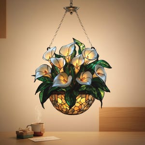 May include: A stained glass hanging lamp shaped like a basket of calla lilies. The lamp features white and yellow flowers with green leaves, and a mosaic-style basket. It hangs from a chain and is illuminated from within.