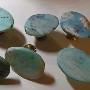 May include: Seven oval-shaped cabinet knobs with a turquoise and brown marbled pattern. The knobs have a polished finish and are mounted on brass or black hardware. These decorative knobs are ideal for adding a unique touch to furniture.