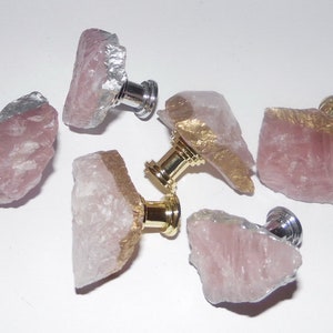 May include: Six pink quartz crystal cabinet knobs with gold and silver accents. The knobs have a raw, natural look and are attached to metal bases.
