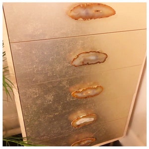 May include: A gold dresser with five drawers and agate stone handles. The dresser has a textured, metallic finish.