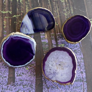 May include: Four purple agate coasters with gold trim. The coasters are round and have a natural, organic shape. They are perfect for adding a touch of elegance to any home.