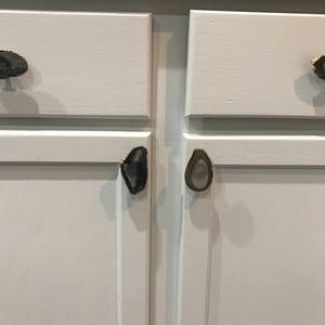 May include: White cabinet doors with agate drawer pulls. The pulls are in the shape of a teardrop and have a gold trim.