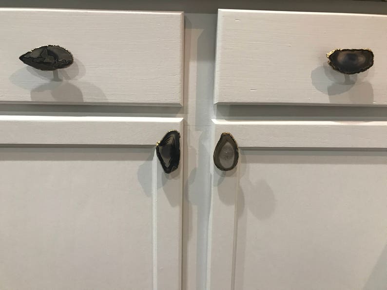 May include: White cabinet doors with agate drawer pulls. The pulls are in the shape of a teardrop and have a gold trim.