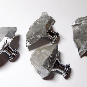 May include: Four clear quartz crystal drawer pulls with silver metal knobs. The crystals are irregularly shaped and have a rough, natural texture.