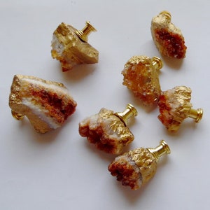 May include: Six gold-painted crystal knobs with a brass screw. The crystals are in various shapes and sizes, with some having a reddish-brown hue.