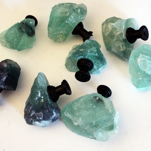 May include: Eight green and black fluorite crystal cabinet knobs with black metal hardware. The knobs are irregularly shaped and have a natural, rough texture.