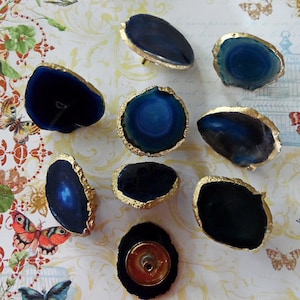May include: Nine agate drawer pulls with gold trim. The agate is a deep blue with white and gray banding. The pulls are approximately 2 inches in diameter.