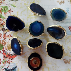 May include: Nine agate knobs with gold trim. The knobs are various shades of blue and have a natural, organic shape.