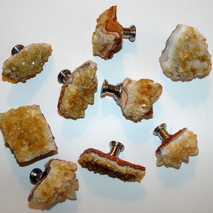 May include: Eight yellow crystal cabinet knobs with silver metal hardware. The knobs are various shapes and sizes, and each has a unique crystal formation.