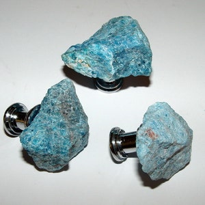 Puede incluir: Tres pomos de cristal azul verdoso con bases plateadas. Los pomos son rugosos y tienen un aspecto natural y sin pulir.