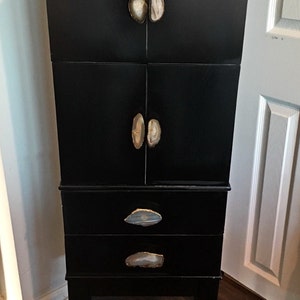 May include: A black cabinet with four drawers and two doors. The cabinet has agate stone handles. The cabinet is standing on a wooden floor.