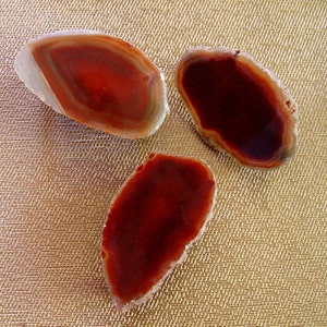May include: Three agate slices with red and brown banding. The slices are translucent and have a natural, organic shape.