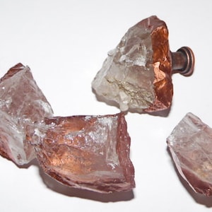 May include: Three clear glass knobs with a copper finish. The knobs are irregularly shaped and have a rough, natural texture.