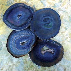 May include: Four blue agate slices with intricate patterns and a natural, polished finish. The slices are arranged in a cluster, showcasing their unique shapes and textures.