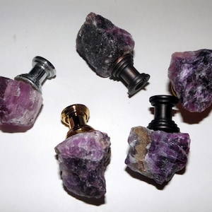 May include: Five purple amethyst crystal cabinet knobs with different metal bases. The knobs are in various shapes and sizes.