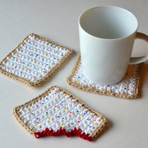 May include: Three crocheted coasters with a white background and colorful sprinkles. The coasters are shaped like a square and a rectangle with a bite taken out of it. A white mug is sitting on one of the coasters.