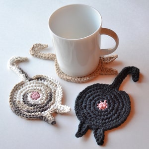 May include: Three crocheted cat butt coasters. One is black, one is brown and white, and one is beige. The coasters are shaped like cat butts with a pink circle in the center of each.
