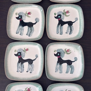 May include: A set of eight square ceramic plates featuring a hand-painted black poodle with a grey pom-pom hairstyle, a red collar, and a small pink flower accent. Each plate has a speckled light green border on a cream-coloured background.