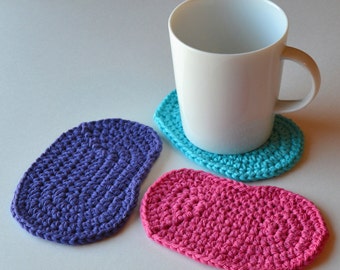 May include: Three crocheted oval coasters in purple, turquoise, and pink. A white ceramic mug sits on top of the turquoise coaster.