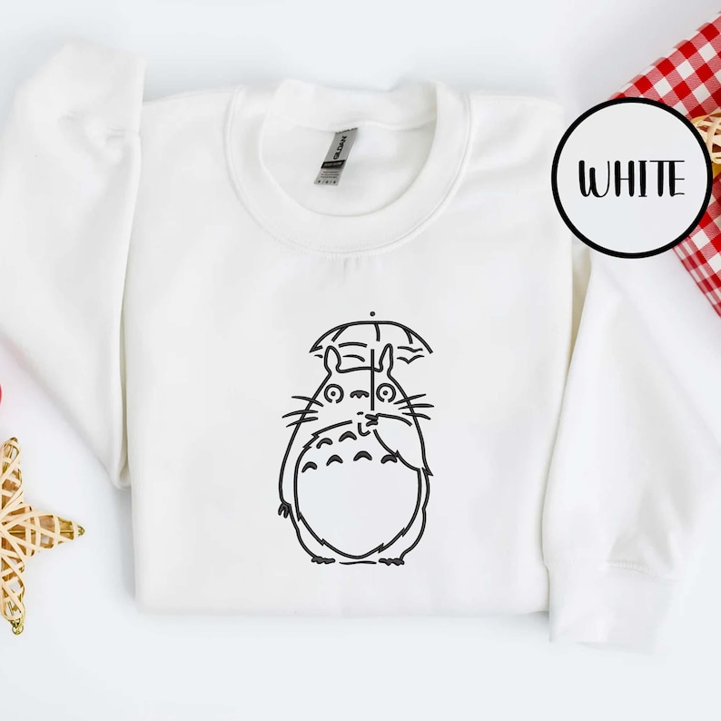 May include: White sweatshirt featuring a black line drawing of a cartoon character holding an umbrella. The word "WHITE" is in a black circle in the upper right corner. The sweatshirt has a crew neck and long sleeves.