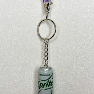May include: A miniature Sprite Zero Sugar soda can keychain. The can is light green and white with the Sprite logo in green. The keychain has a silver chain, a key ring, and a purple clasp.