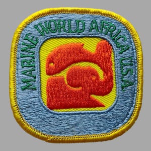 May include: A blue and yellow embroidered patch with the text "Marine World Africa USA" and a red and yellow stylized image of a whale and an elephant.