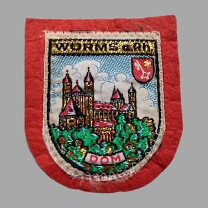 May include: A red, shield-shaped patch with an embroidered design. The design features a detailed illustration of a castle with red roofs, green trees, and the text "WORMS a Rh" and "DOM".