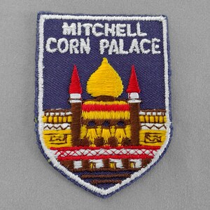 May include: A blue embroidered patch with white text that reads "Mitchell Corn Palace". The patch features a yellow and red building with a yellow dome.
