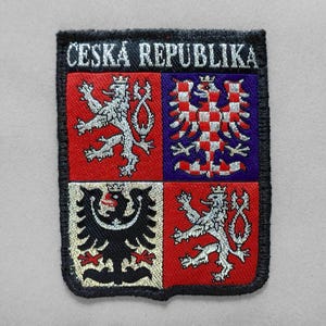 May include: A rectangular embroidered patch featuring the coat of arms of the Czech Republic. The design is divided into four quadrants with red, blue, and white colors, displaying a double-tailed lion and a checkered eagle. The text CESKÁ REPUBLIKA is stitched in white at the top.