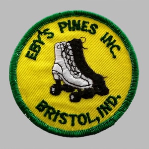 May include: Embroidered patch with a yellow center, green border, and the text "EBY'S PINES INC. BRISTOL, IND." in green. The patch features a white and black roller skate design.