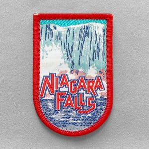 May include: A rectangular patch with a red border features a Niagara Falls design. The patch displays the words "Niagara Falls" in red, with a waterfall illustration in blue and white. The patch is likely an embroidered souvenir.