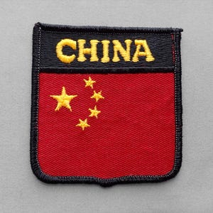 May include: A rectangular embroidered patch featuring a red background with five yellow stars arranged in a pattern on the left side. The top section is black with the word CHINA stitched in yellow capital letters, all bordered by black thread.