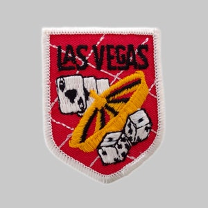May include: Red and white embroidered patch with the text "LAS VEGAS" in black. The patch features a yellow and black playing card chip, playing cards, and dice.