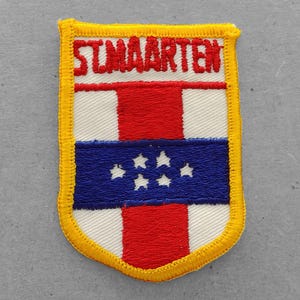 May include: A yellow, white, red, and blue embroidered patch with the text "ST. MAARTEN" in red. The patch features the flag of Sint Maarten.