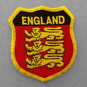 May include: A red and yellow embroidered patch with the word "ENGLAND" in black lettering and three gold lions on a red background.