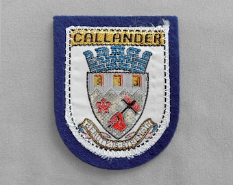May include: A blue and white embroidered patch with the word "CALLANDER" at the top. The patch features a coat of arms with a castle, flowers, and the words "BEAUTY & STRENGTH".