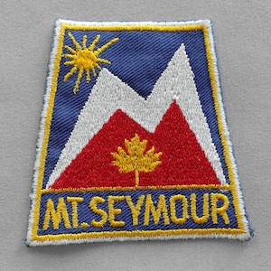 May include: Embroidered patch featuring a mountain scene with a sun and a maple leaf. The patch has a blue background with white and red mountains. The text "MT. SEYMOUR" is in yellow.