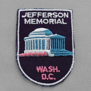 May include: A purple and white embroidered patch with the text "JEFFERSON MEMORIAL WASH. D.C." and a white and blue embroidered image of the Jefferson Memorial building.