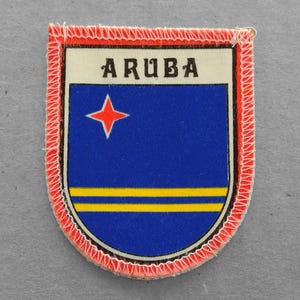 May include: A red, white, and blue fabric patch with the word "ARUBA" and a red star in the upper left corner. The patch is surrounded by a red stitched border.