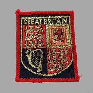 May include: Embroidered patch featuring the words "GREAT BRITAIN" above a heraldic design. The patch has a red border and a black background. The design includes gold and red elements, such as lions, harps, and other symbols.