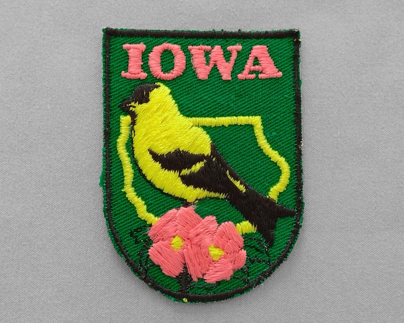 Used vintage Iowa patch with state bird American goldfinch and state flower wild rose embroidered in pink yellow and black on a dark green twill background