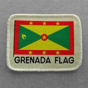 May include: A white patch with a red, yellow, and green Grenada flag design. The flag has a yellow field with a green, red-edged, isosceles triangle pointing down. The triangle has a small yellow five-pointed star in the center. There are six yellow five-pointed stars on the red field above the triangle. The text "GRENADA FLAG" is printed in black below the flag.