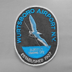 May include: Embroidered patch with the text "Wurtsboro Airport N.Y." in blue, surrounding a black oval. The patch features a blue and white bird in flight and the text "Oldest U.S. Soaring Site Established 1927."