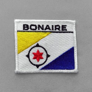 May include: A square embroidered patch featuring the flag of Bonaire with the word BONAIRE in black text at the top. The design includes a yellow triangle, a white field, and a blue triangle, with a black compass rose and a red six-pointed star.