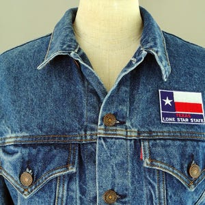 May include: A blue denim jacket with a patch on the left chest that reads "Texas Lone Star State" and features a red, white, and blue Texas flag.