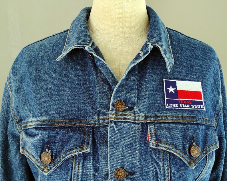 May include: A blue denim jacket with a patch on the left chest that reads "Texas Lone Star State" and features a red, white, and blue Texas flag.