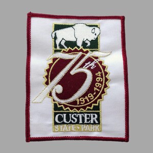 May include: Embroidered patch featuring a white bison above a burgundy and gold emblem with the text "75th 1919-1994". The patch has a white background with a red border and the words "Custer State Park" at the bottom.
