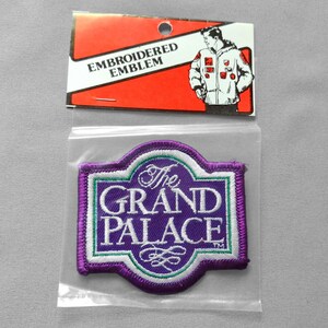 May include: Embroidered emblem in a plastic bag. The purple patch features the words "The Grand Palace" in white, with a green and white border. The emblem is in a plastic bag with a red and white tag that reads "Embroidered Emblem".